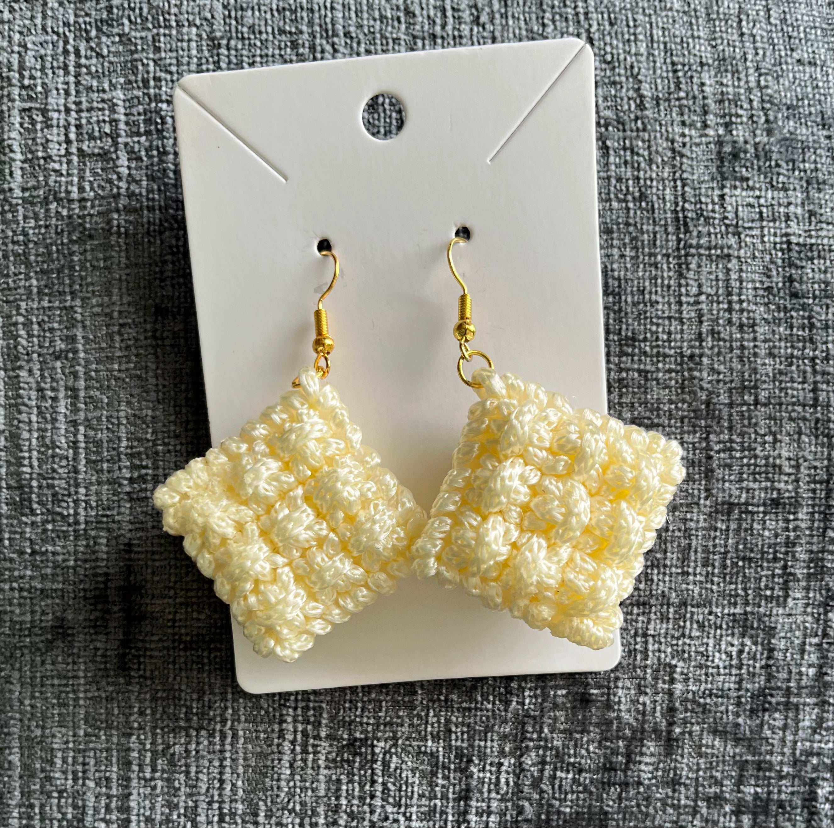 Pair of beige crocheted earrings on a white card against a textured gray background